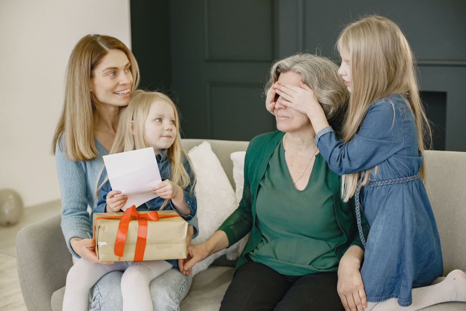 Nietas, hija y abuela celebran el Día de la Madre entre risas con regalos en un sofá todas sentadas. 