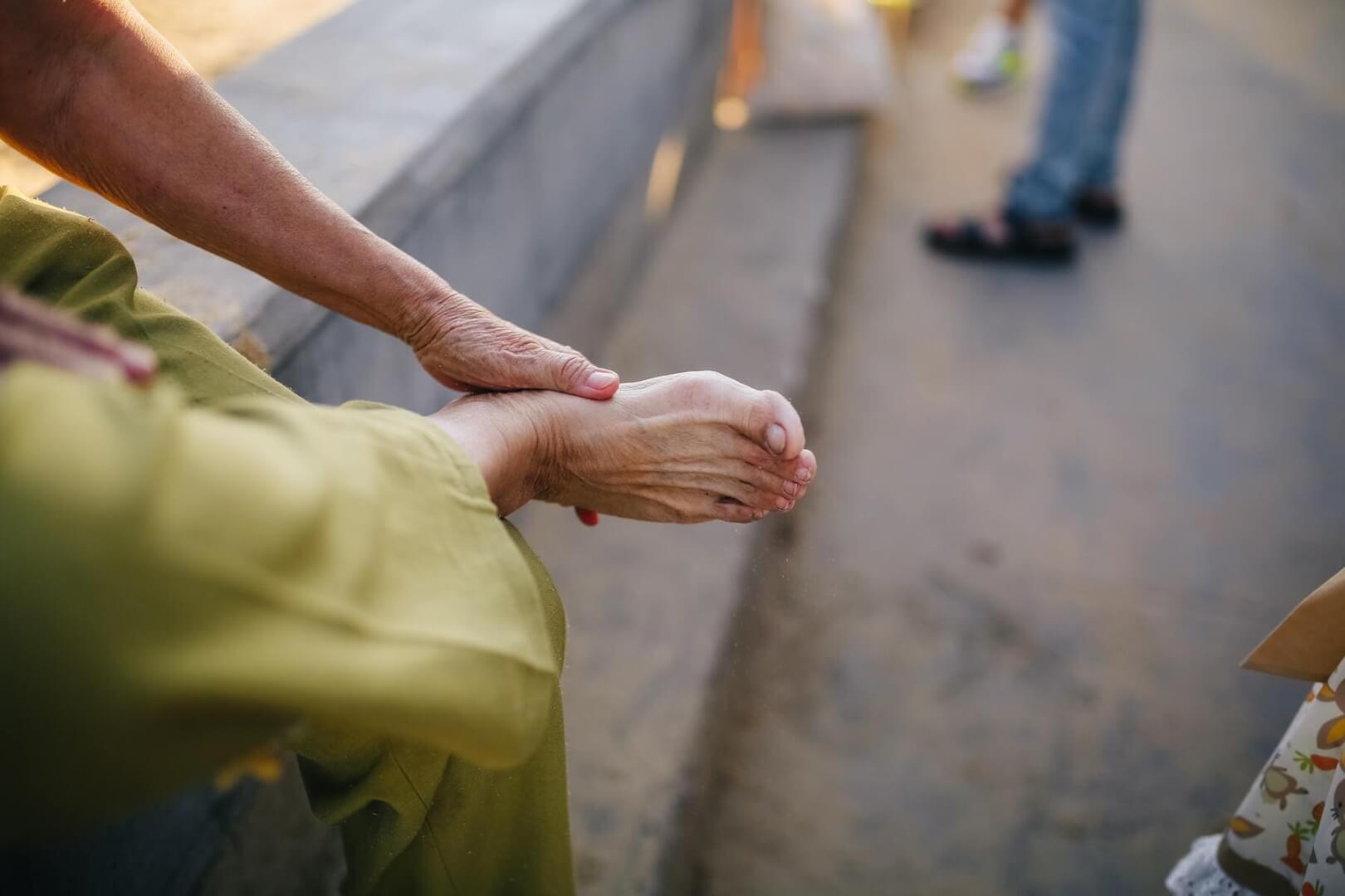 Una mujer mayor sentada se toca la planta del pie. 