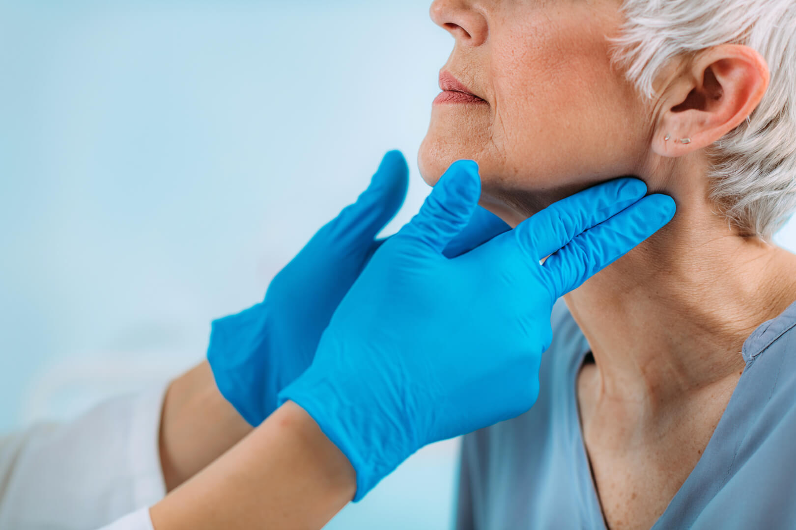 Un médico examina la glándula de la tiroides a una señora mayor.