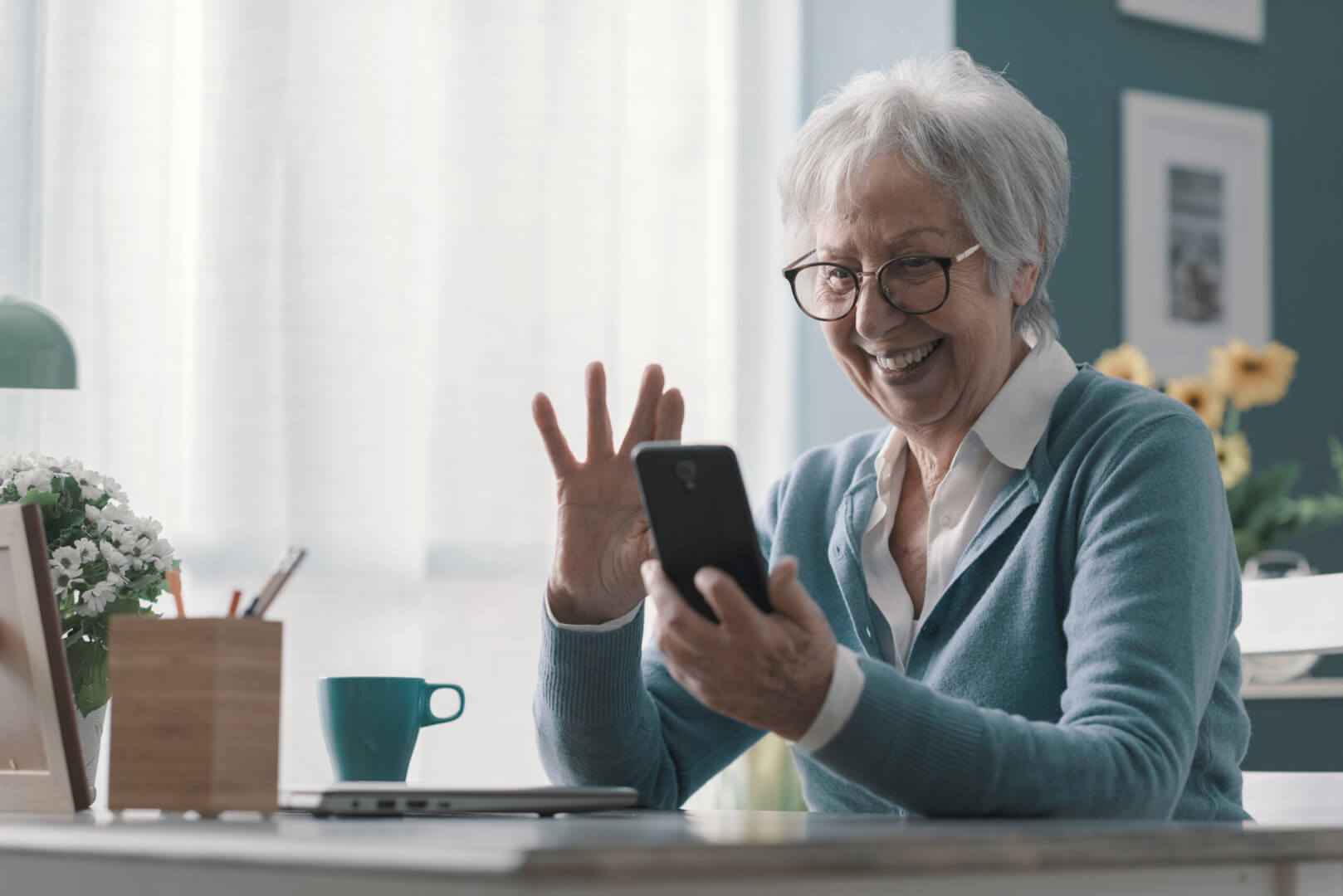 Una anciana usa su smartphone para interactuar con otros usuarios en una red social. Está saludando con su mano.