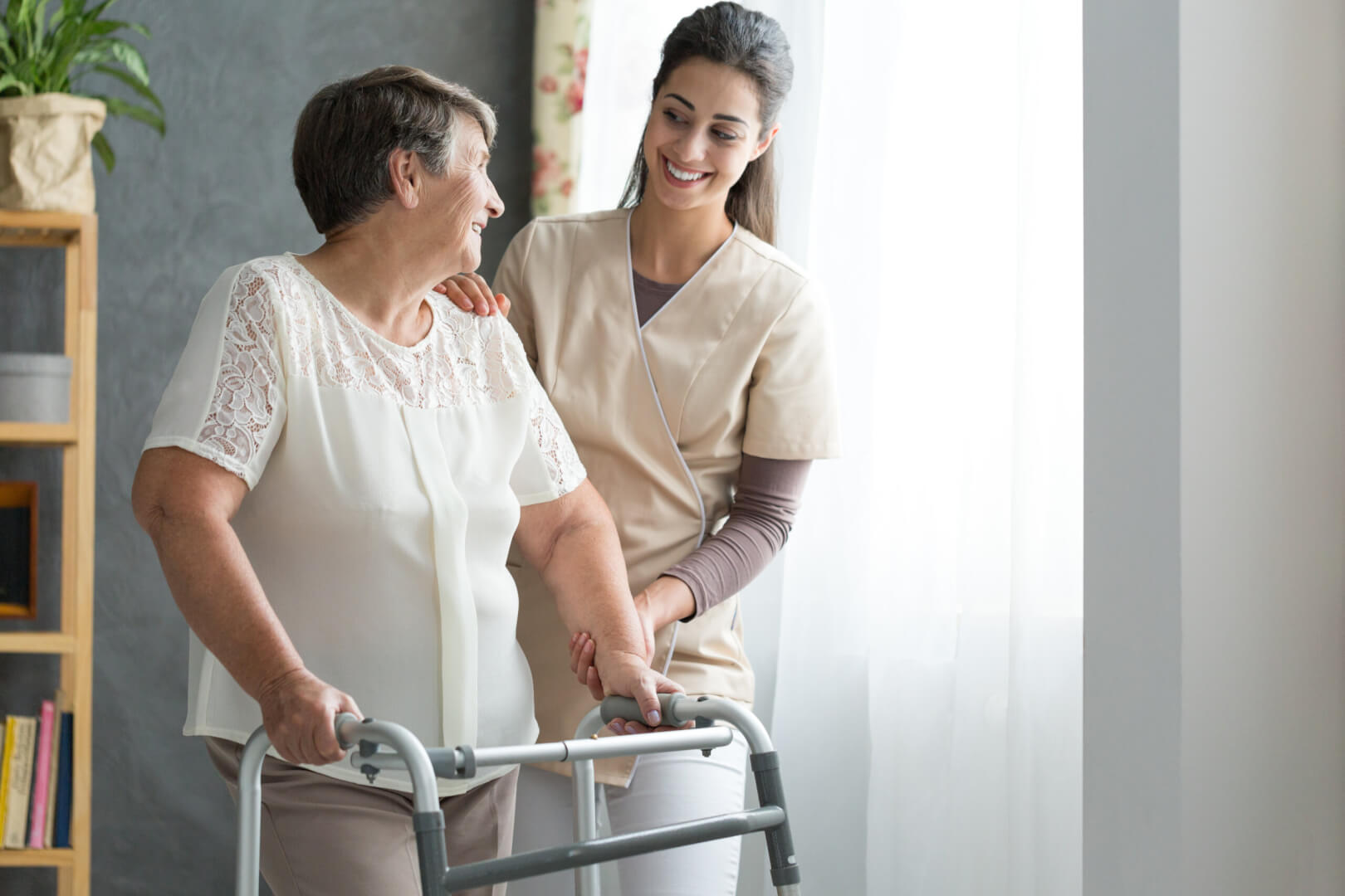 Una cuidadora ayuda a una mujer mayor en casa después de sufrir ésta una fractura de cadera y necesitar un andador. 
