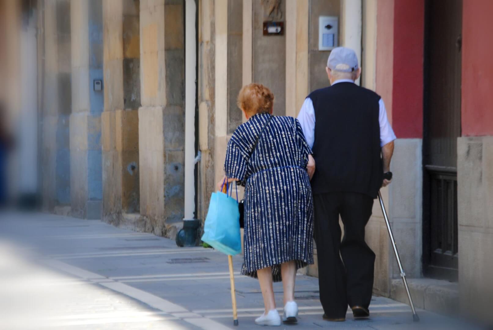 Dos ancianos caminan por una calle cogidos. 