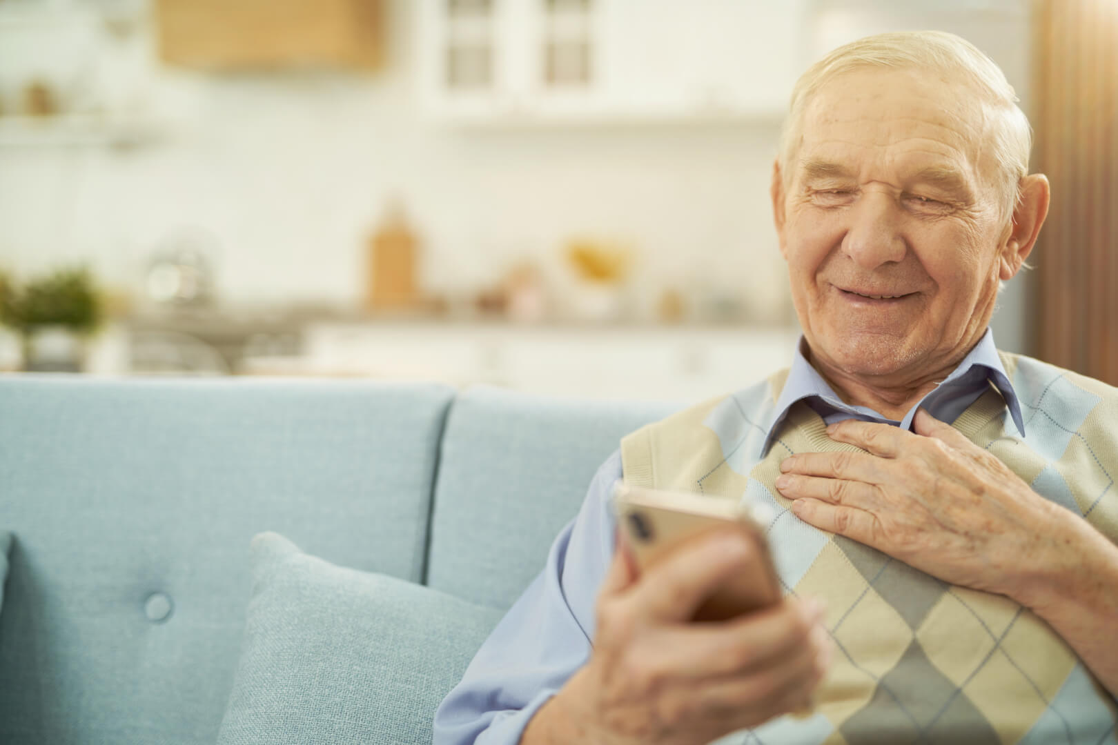 Un hombre mayor se divierte viendo vídeos de TikTok con su smartphone en el sofá de su casa.