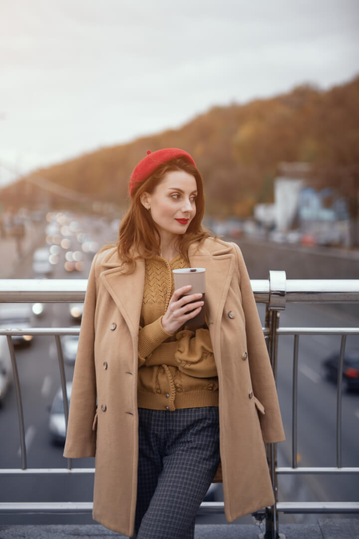 Una chica joven en un puente de un municipio posa con un café y una boina roja.