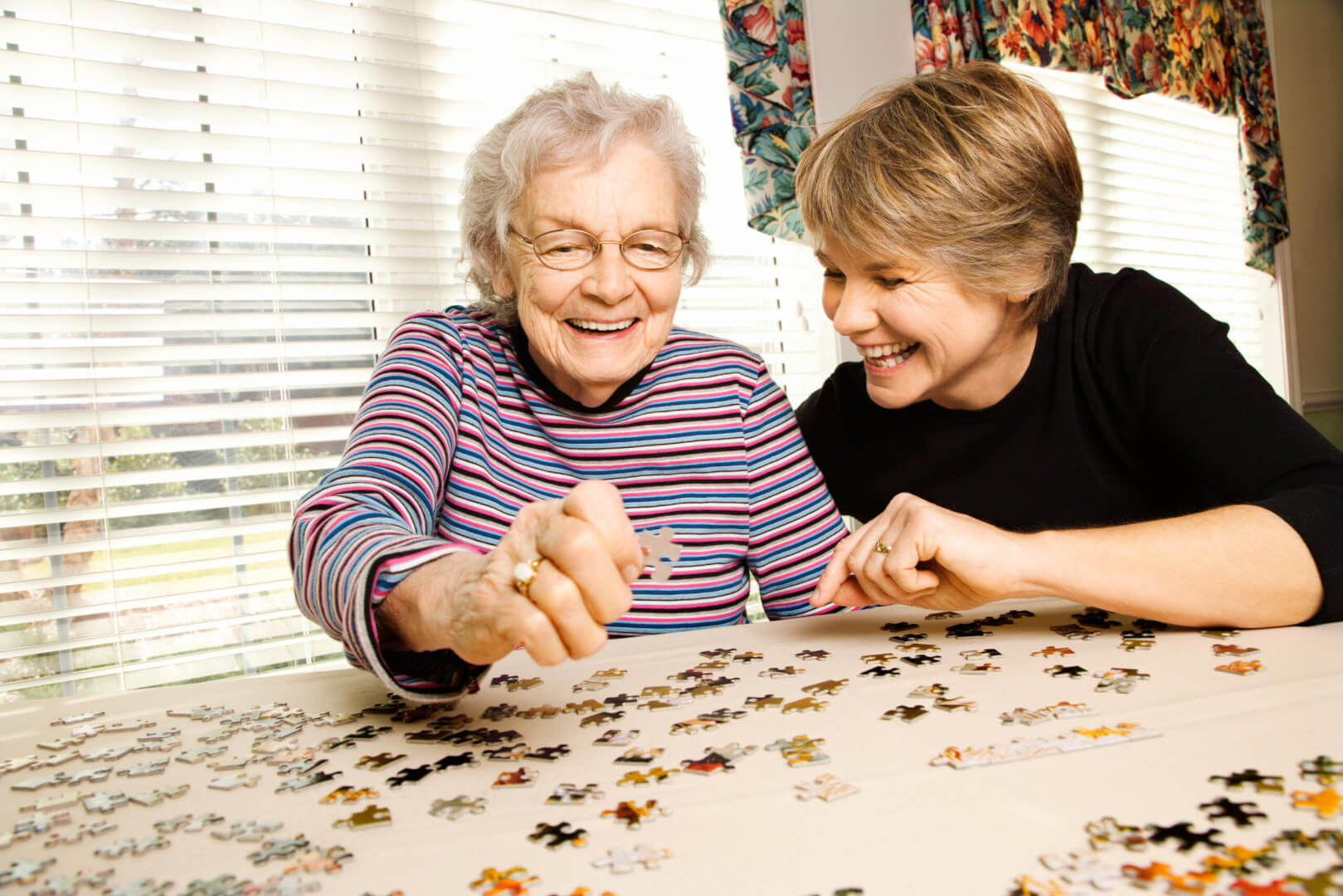 Una cuidadora ayuda a montar un puzzle en una mesa a una señora mayor que padece alzhéimer.