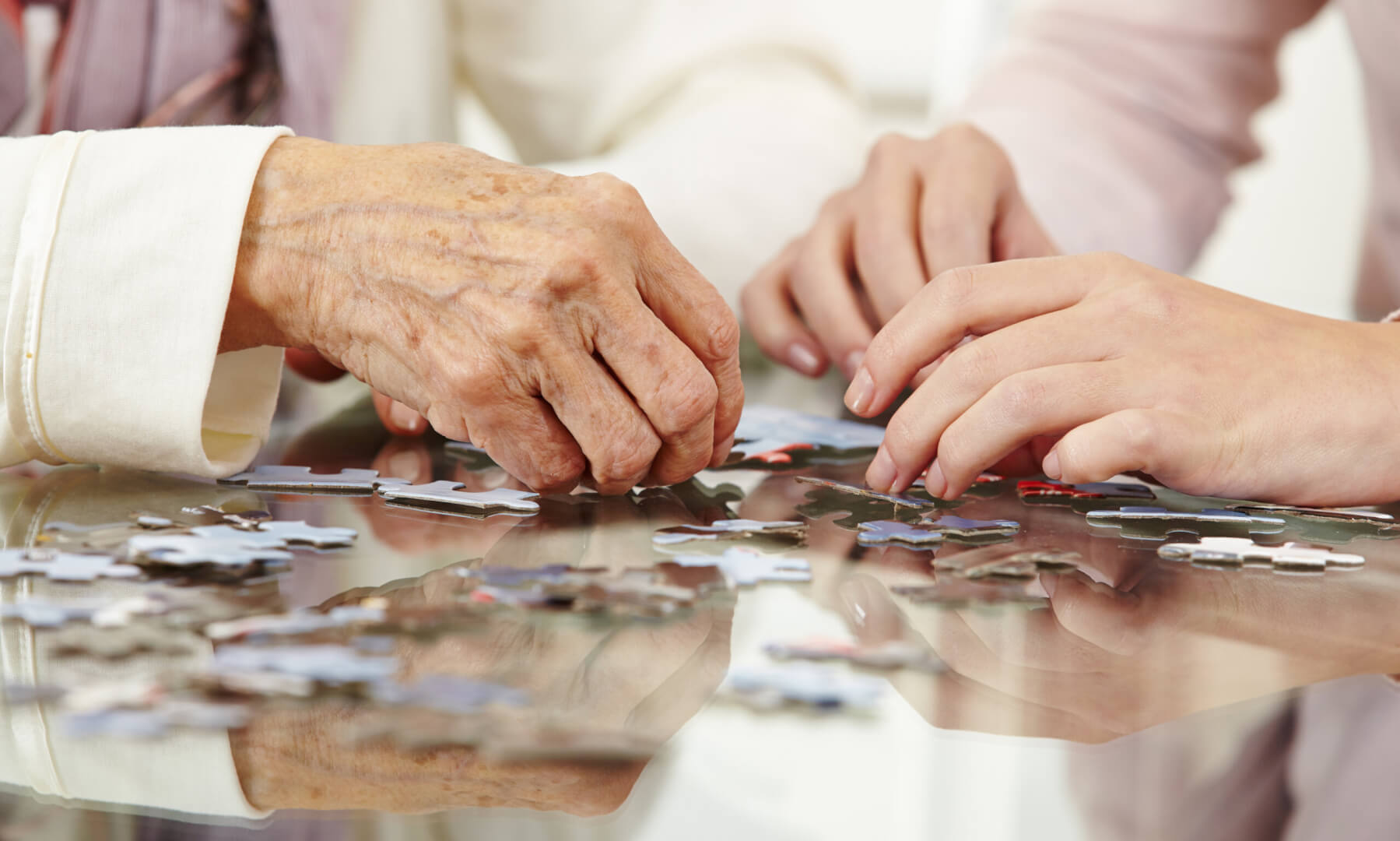 Un plano detalle de unas manos de una cuidadora ayudando a una señora mayor a realizar un puzzle