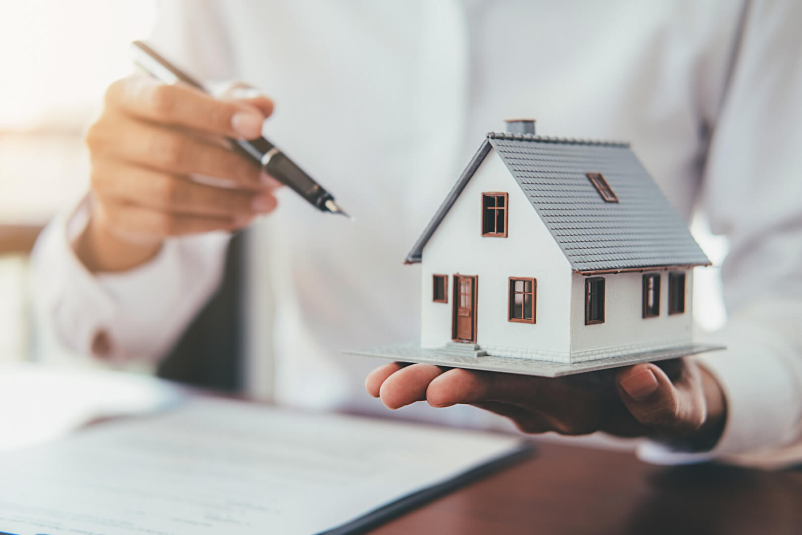 Una imagen de una persona sosteniendo un bolígrafo y una maqueta de una casa simbolizando la compra de una vivienda