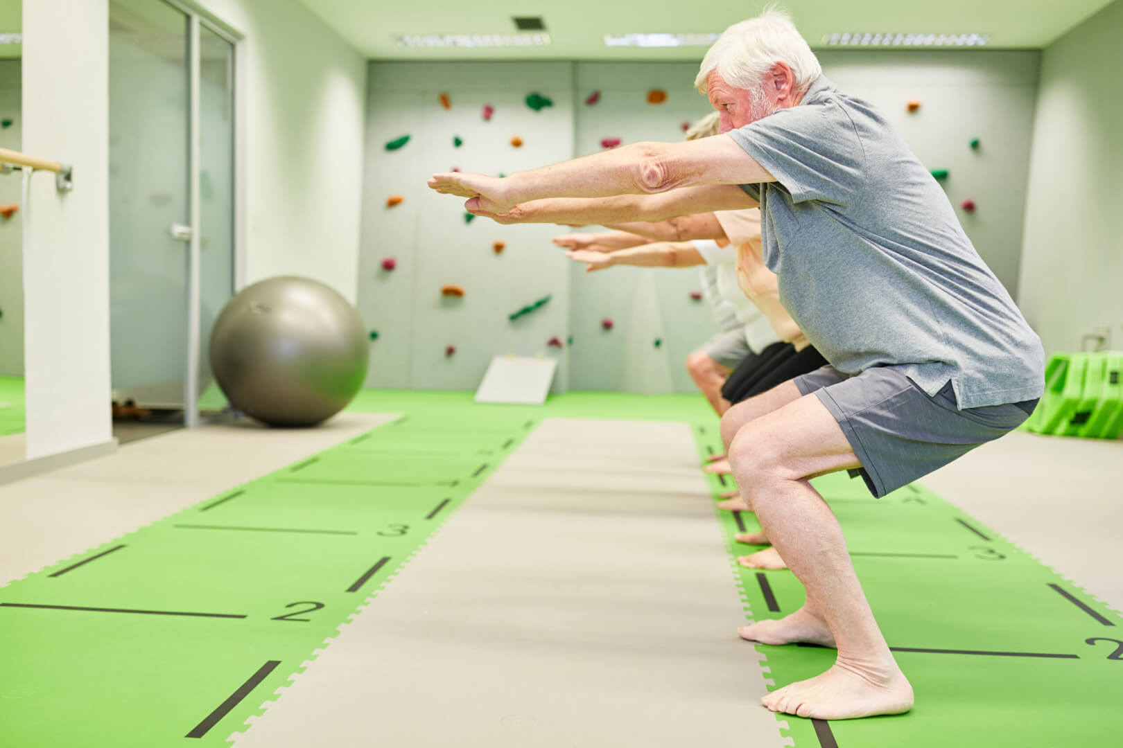 Un señor mayor realiza un paso básico de zumba mediante sentadillas en un gimnasio.