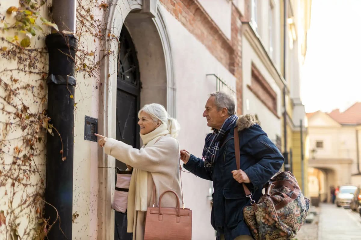 Una pareja de más de 65 años tocando un timbre para entrar a un alojamiento turístico