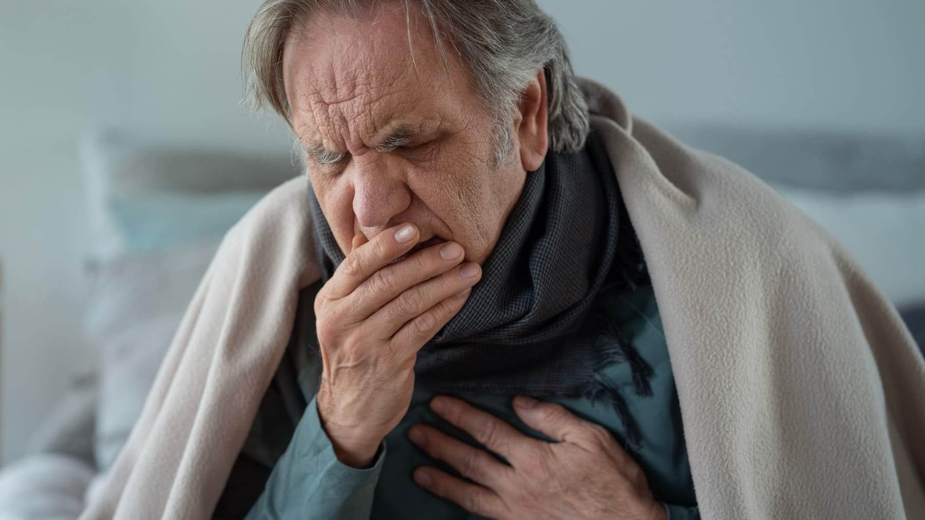 Un hombre tapado tosiendo. 