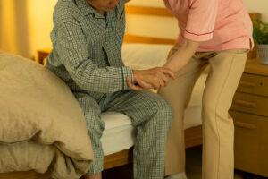 Cuidadora ayuda a hombre mayor con pijama a sentarse en la cama.