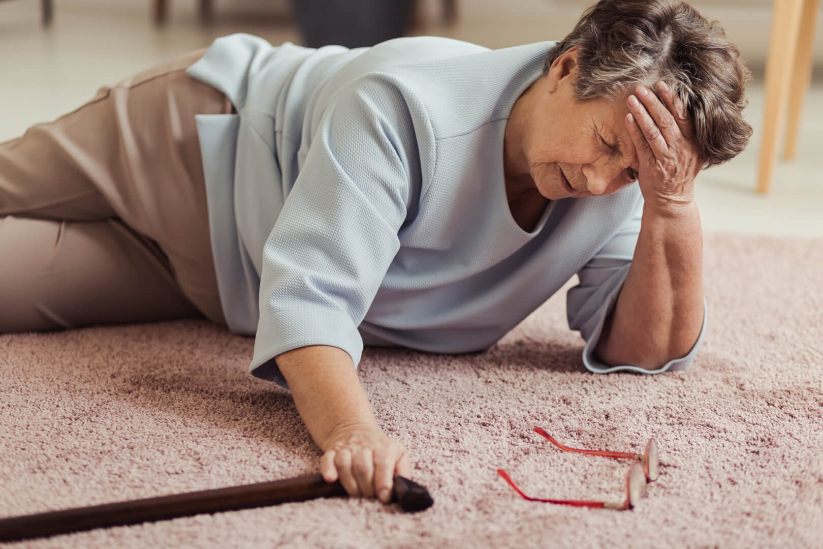 Una anciana se queja del dolor de cabeza tras una caída en la alfombra de su casa.