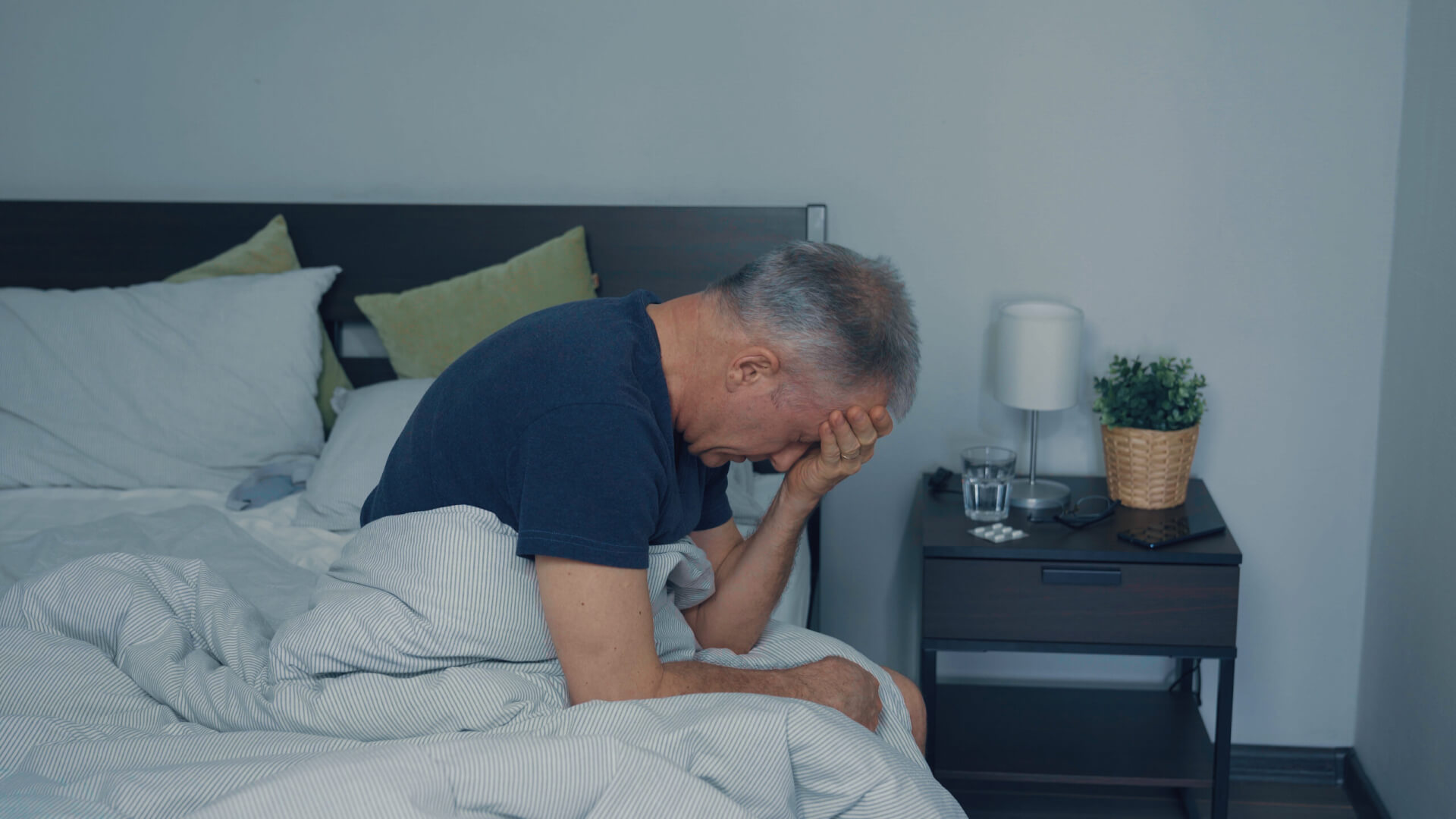 Un hombre mayor se siente mareado al levantarse por la mañana en su cama.