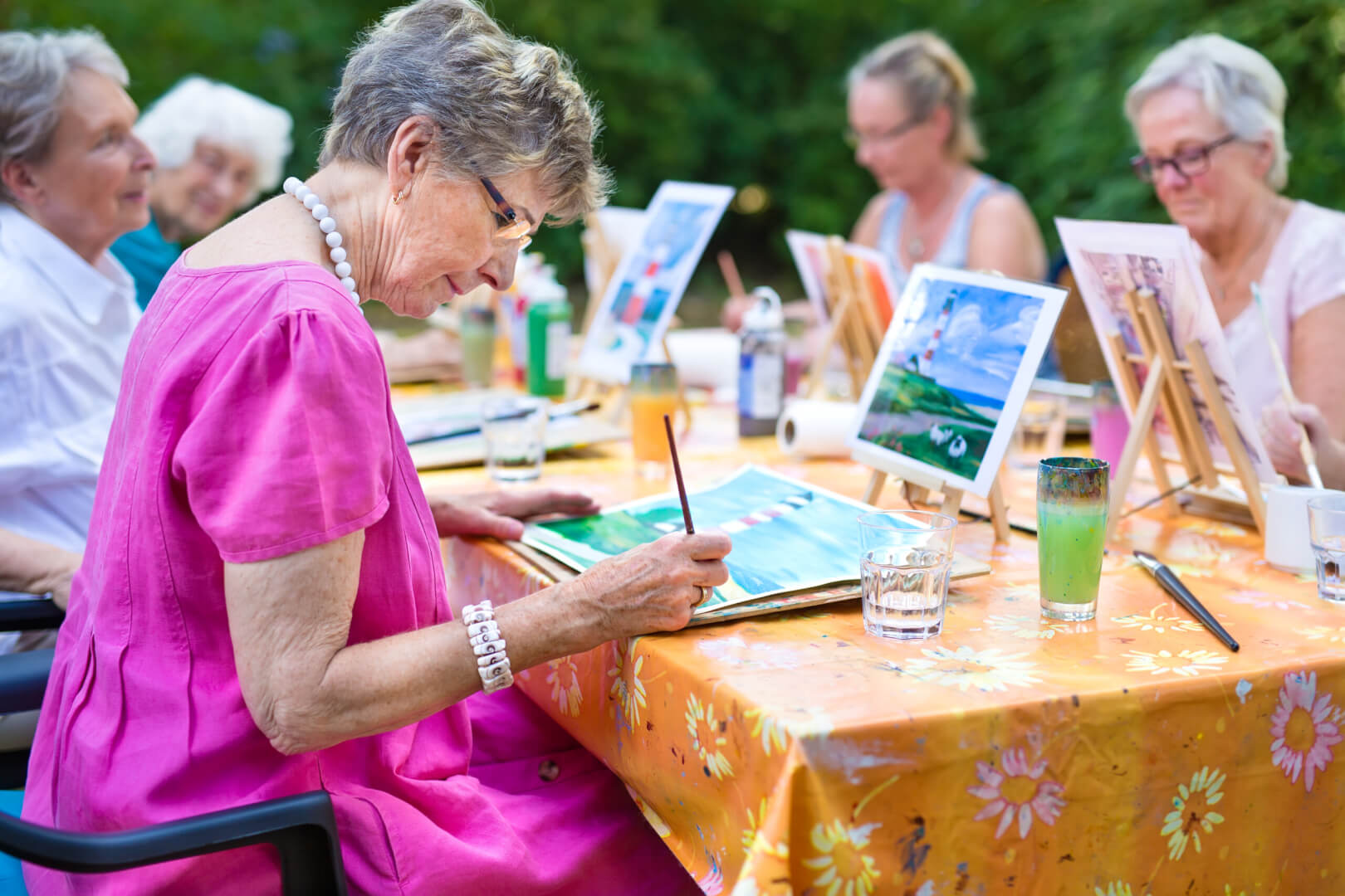Unas mujeres mayores pintan sobre una mesa unos cuadros.