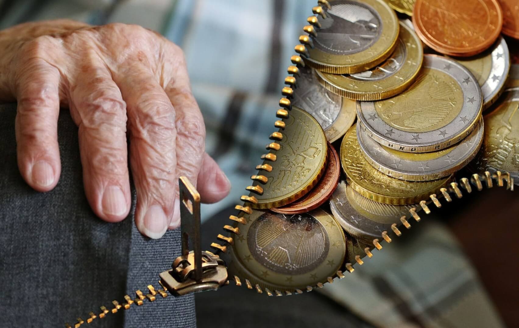 Una manos de un señor mayor abren una cremallera donde hay monedas de euro.