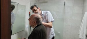 Un cuidador ayuda a señor mayor mientras este se ve en el espejo del baño.