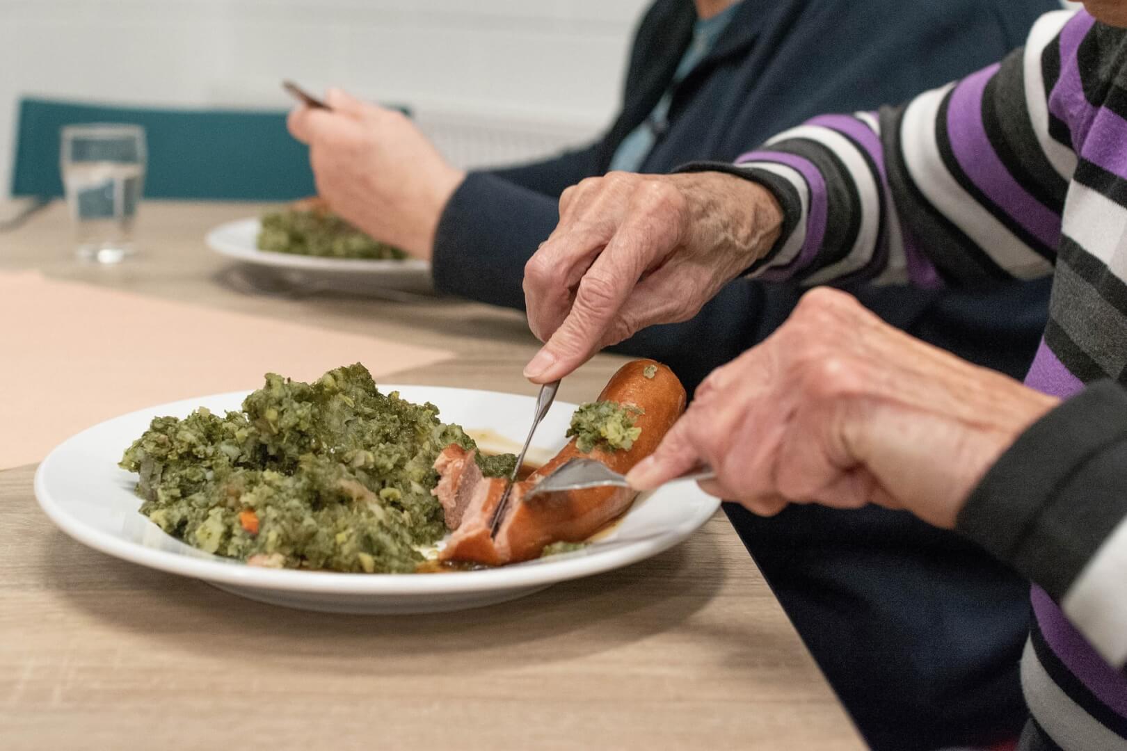Un plano corto de un anciano comiendo un plato de comida con alto valor en colesterol.