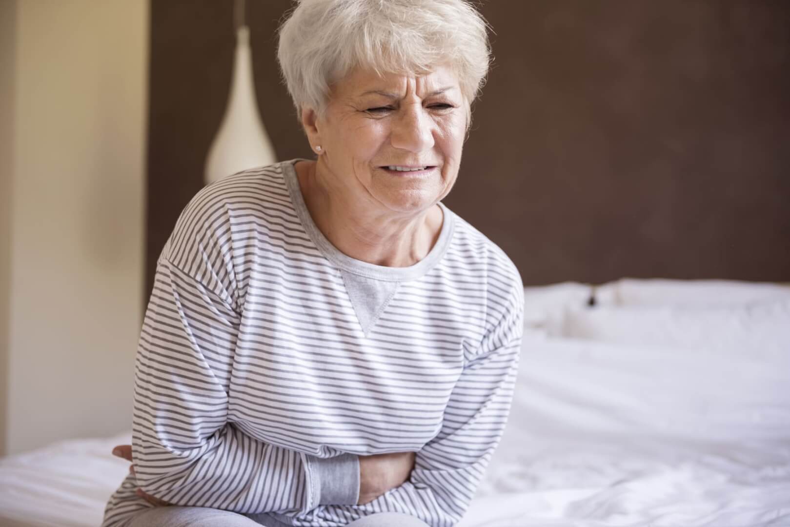 Una mujer mayor se toca el estómago en su cama en claro síntoma de dolor.