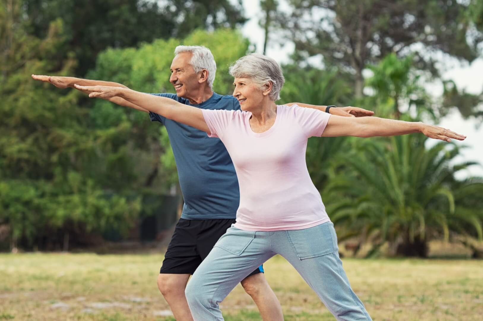 Dos ancianos practican yoga y posturas en un parque.