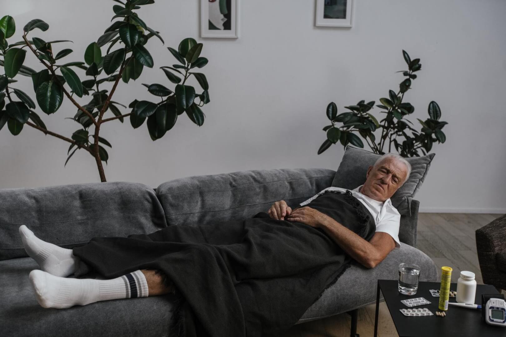 Un anciano postrado en el sofá de su casa con una manta.