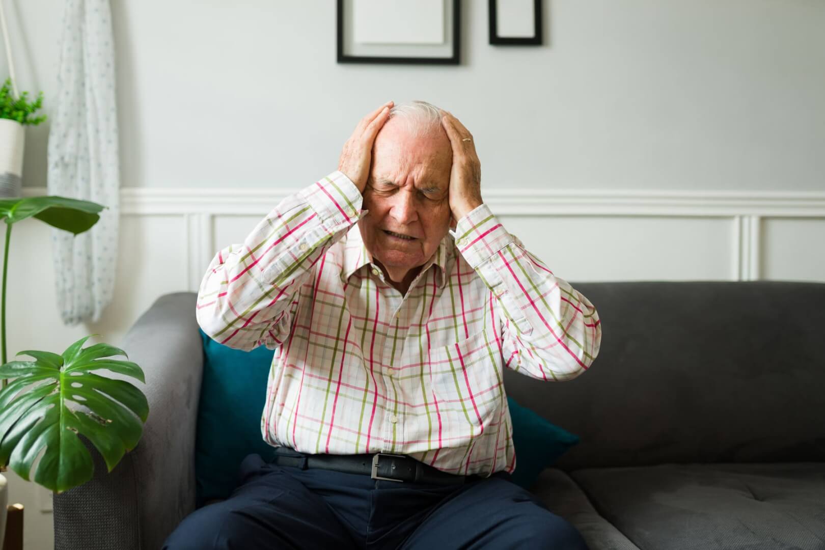 Un anciano en el sofá de su casa con dolor de cabeza.