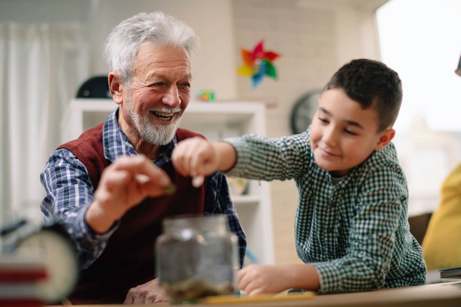 Un abuelo introduce una moneda con su nieto en una hucha. 