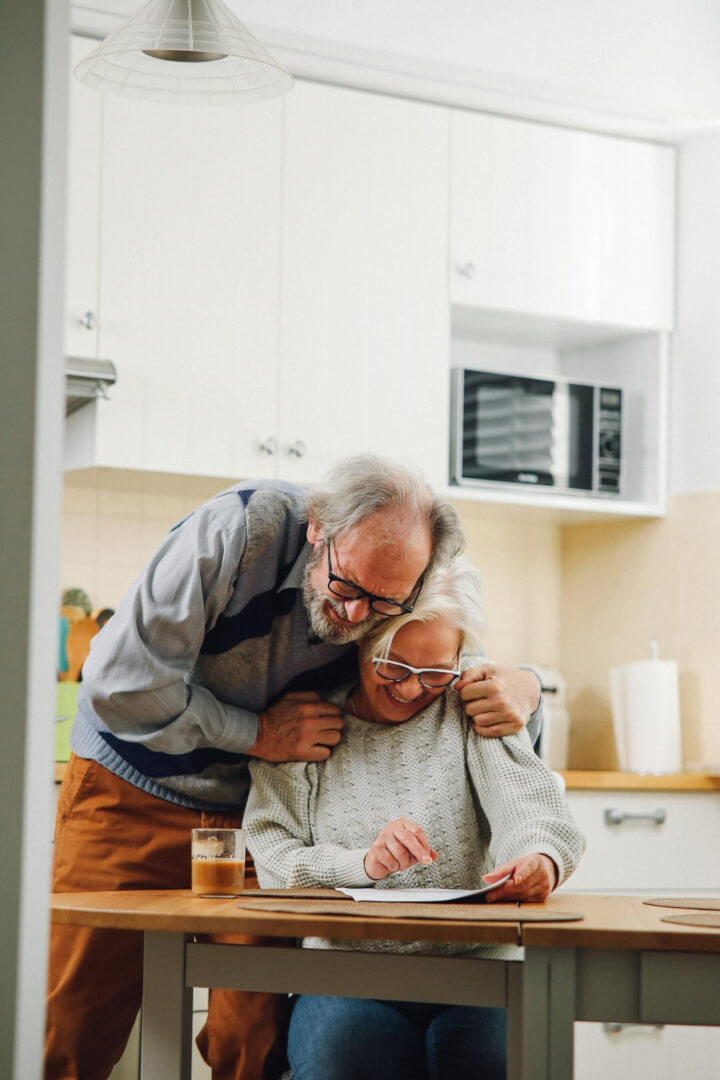 Una pareja de ancianos celebran una buena noticia mientras leen un papen en la cocina de su casa.
