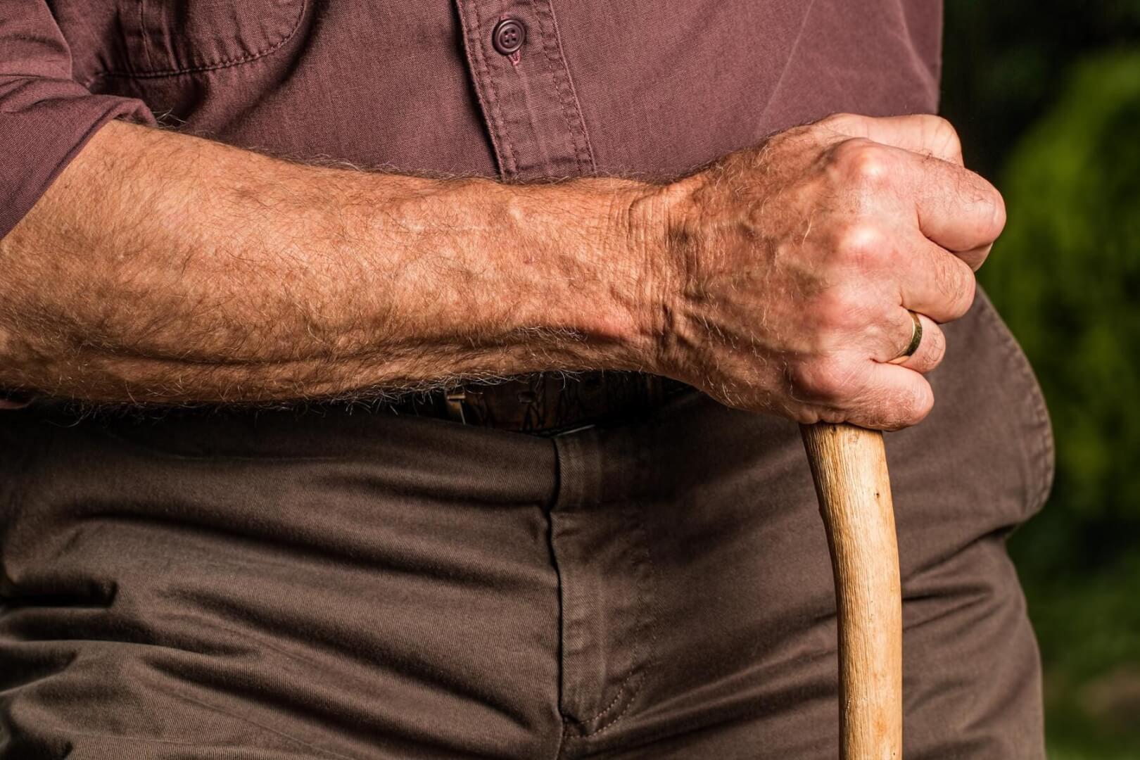 Un plano detalle del brazo de un anciano con un bastón. 