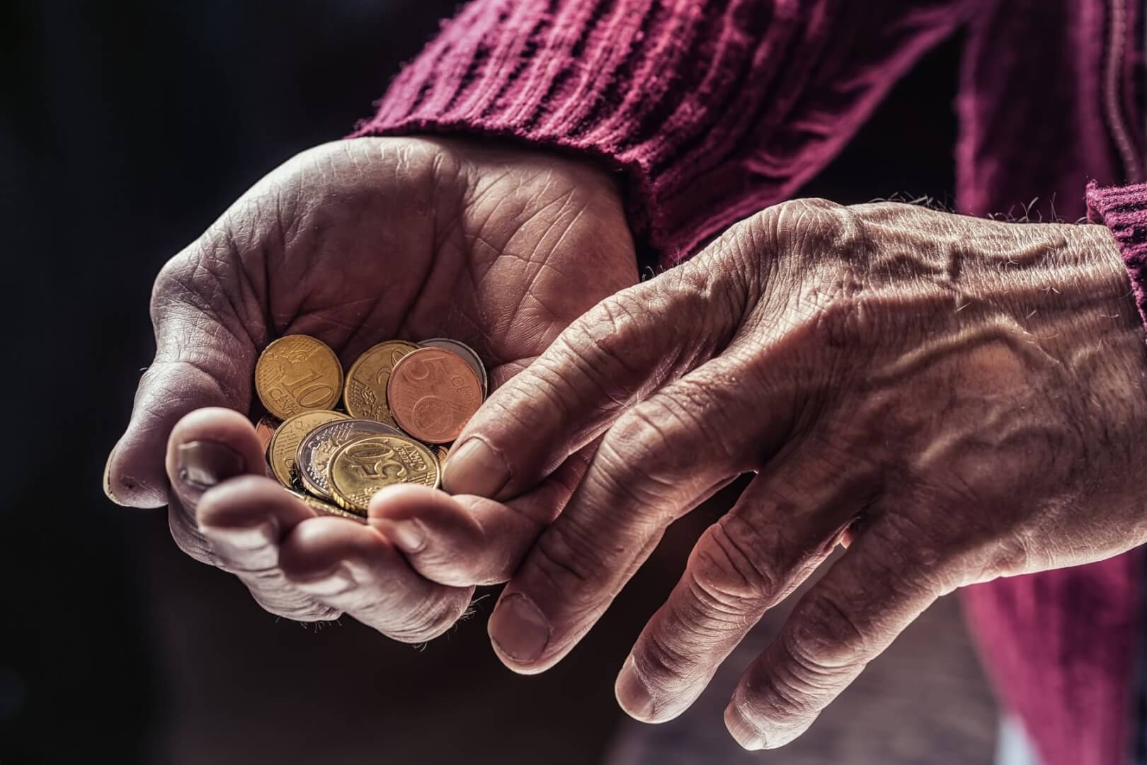 Una imagen de unas manos en detalle de un ancianos con unas pocas monedas de euros. 