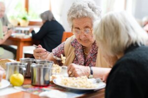 Una mujer mayor con un tenedor en la mano comiendo junto a otra persona mayor
