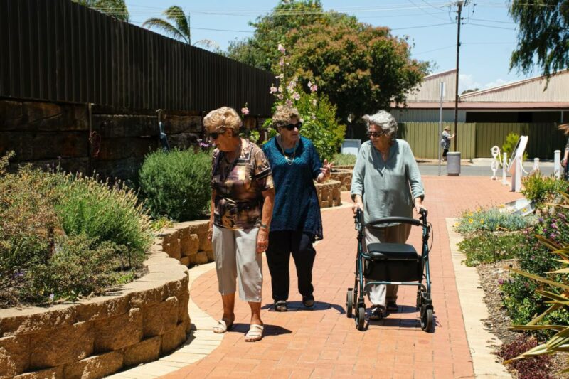 Tres mujeres mayores pasan por un parque mientras conversan. 