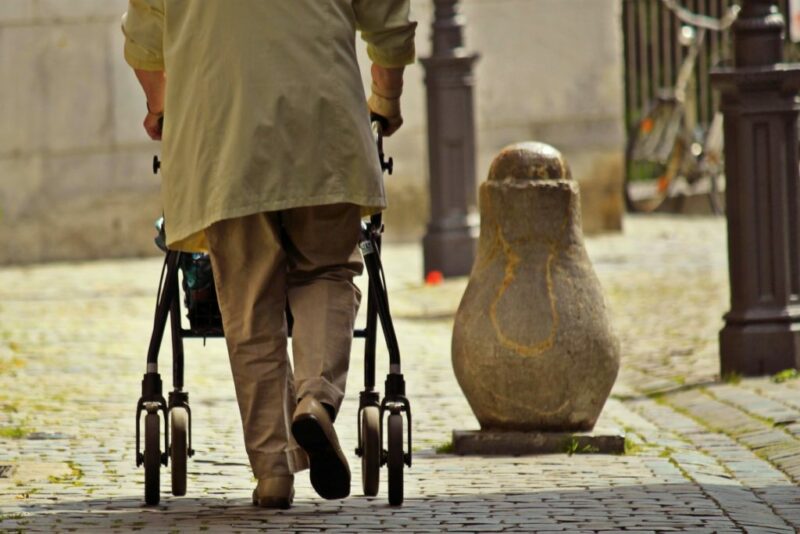 Persona mayor se apoya para caminar en un andador con ruedas.