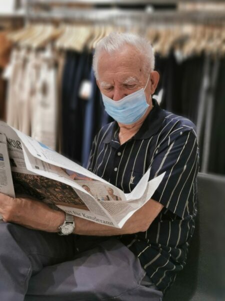 Persona mayor leyendo el periódico ataviado con una mascarilla. 