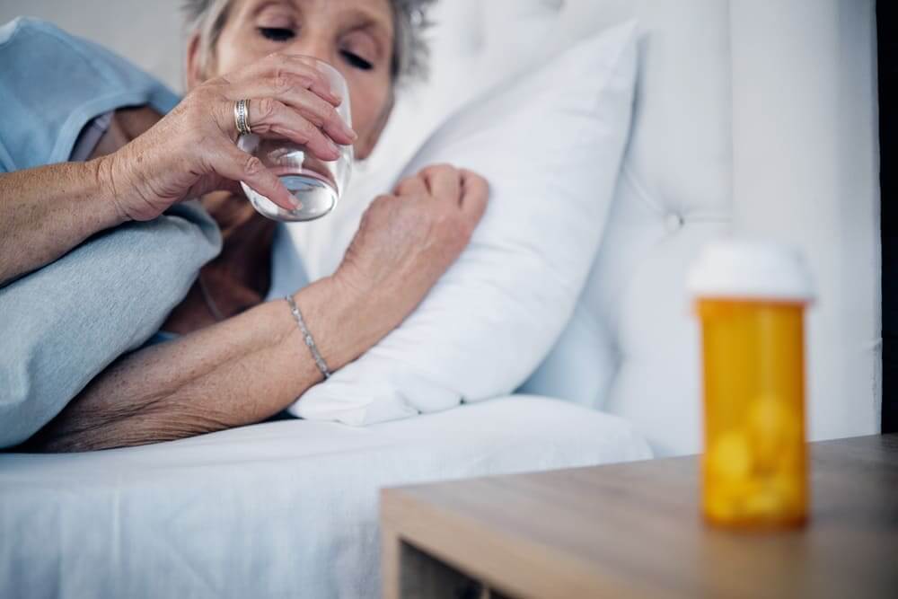 Una mujer mayor toma un vaso de agua tras haber tomado una pastilla par dormir. 