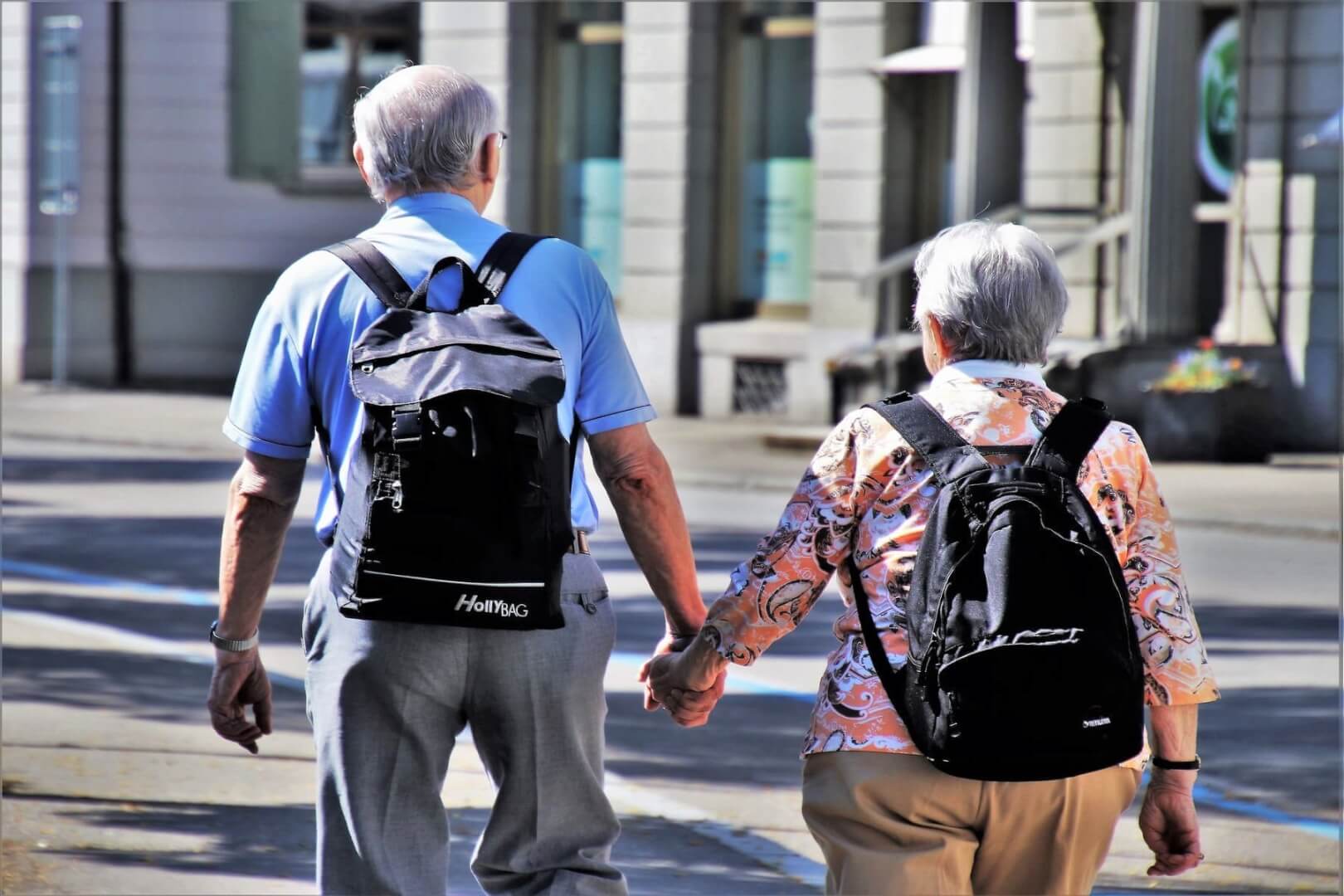 Dos personas mayores cogidas de la mano andando. Están realizando viajes del IMSERSO