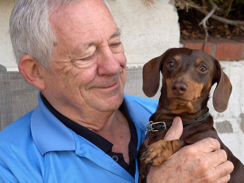 Foto de un anciano feliz con un perro salchicha en sus brazos.