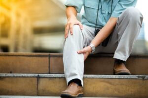 Un hombre sentado en una escalera con la mano en una de sus pantorrillas, como si tuviera dolor en ella.