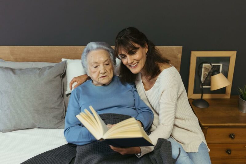 Una cuidadora ayuda a leer un libro a una mujer mayor.