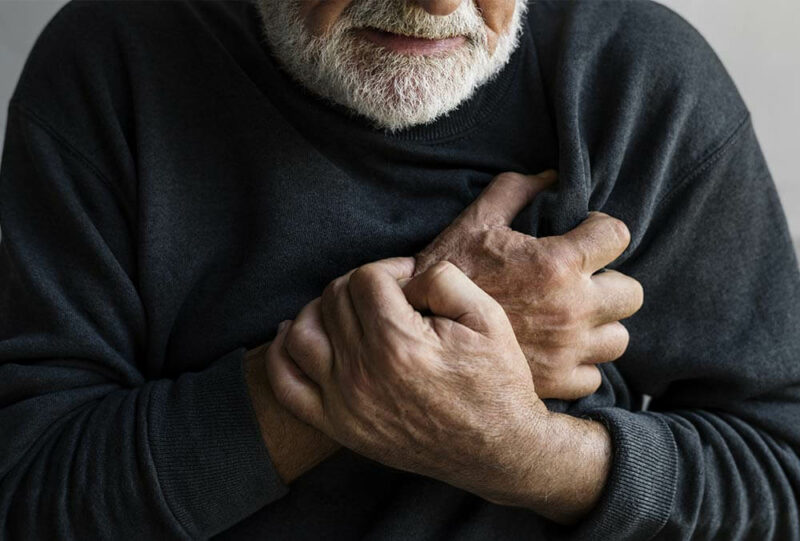 Adulto mayor se lleva la mano al corazón y tiene cara de preocupación.
