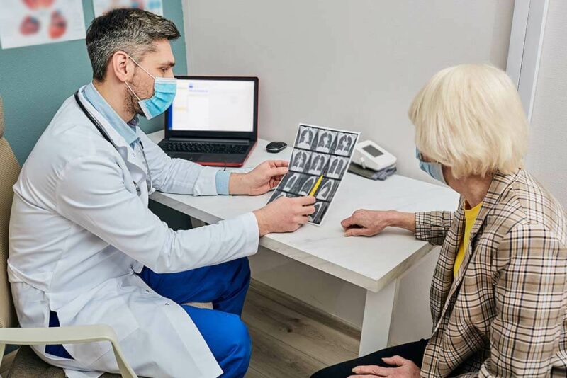 Doctor explica a mujer mayor las secuelas de la fibrosis quística en sus pulmones en una radiografía.