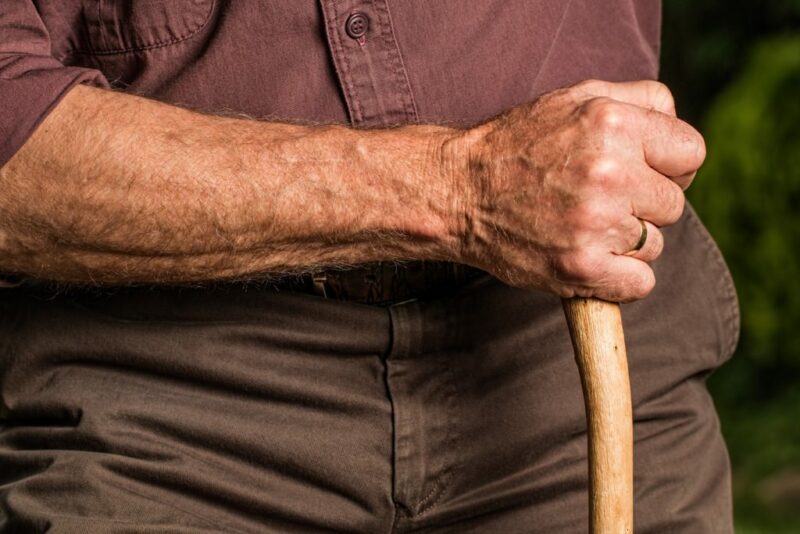 Primer plano de la piel del brazo de un anciano apoyado en un bastón.