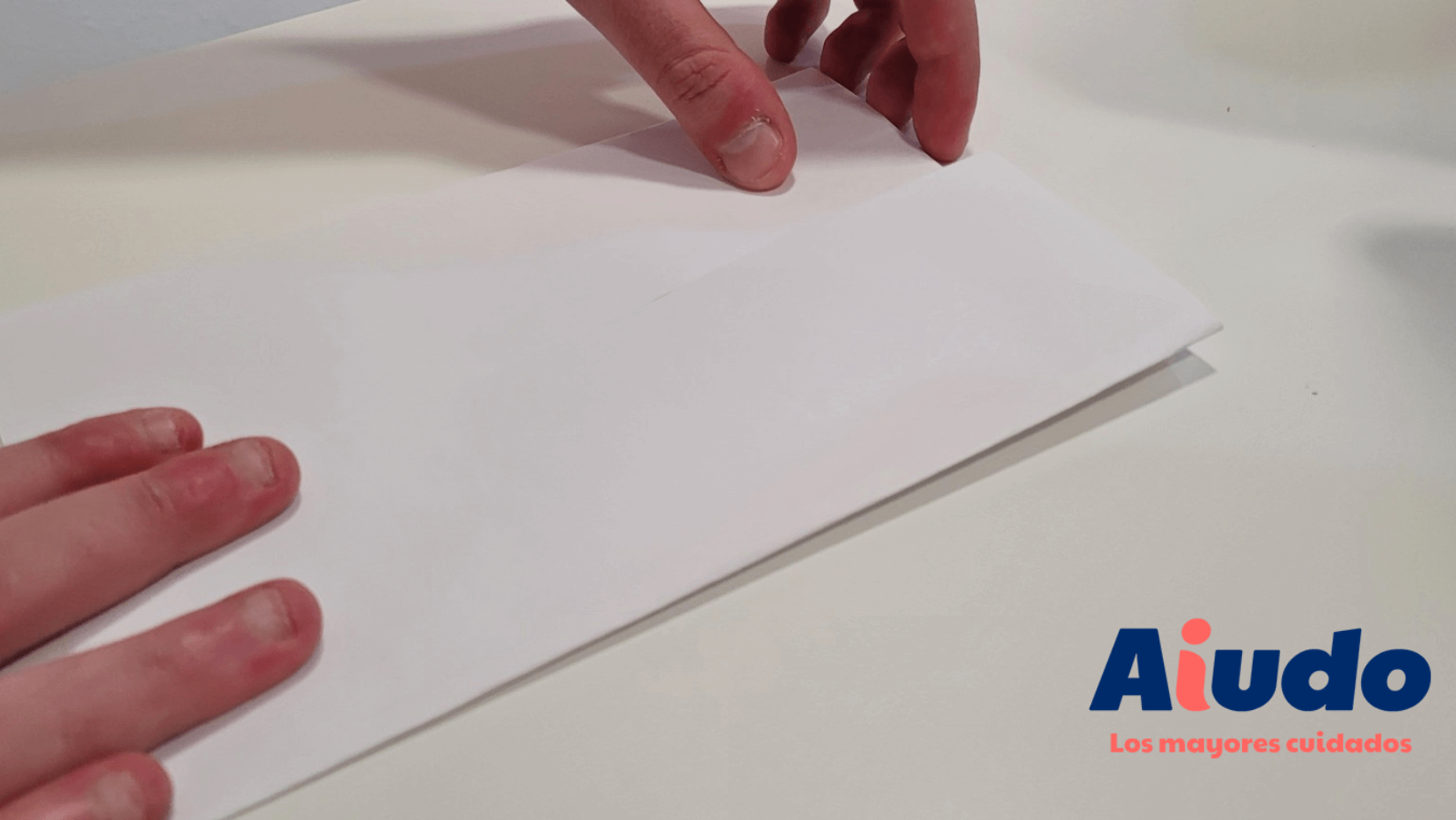 Unas manos pliegan un folio en un paso de una manualidad, en concreto, un abanico de papel.