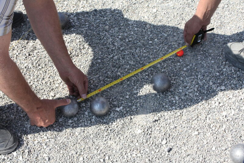 Una pareja de abuelos miden con un metro la distancia entre las bolas de petanca. 