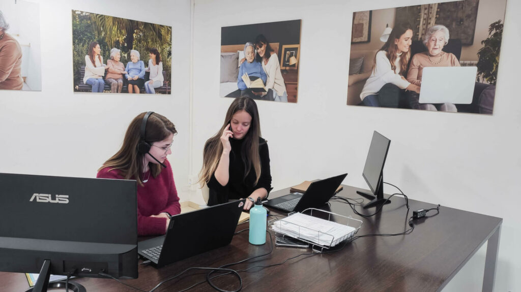 2 mujeres sentadas, trabajando en Aiudo con auriculares, en una sala con cuadros.
