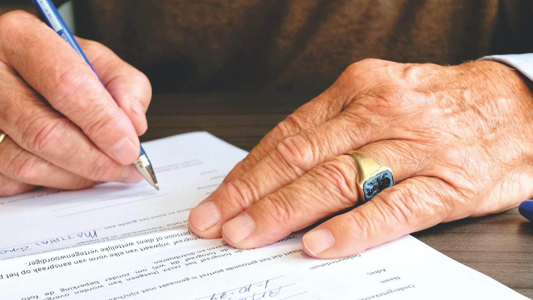 Un plano detalle de unas manos de un anciano firmando un documento. 