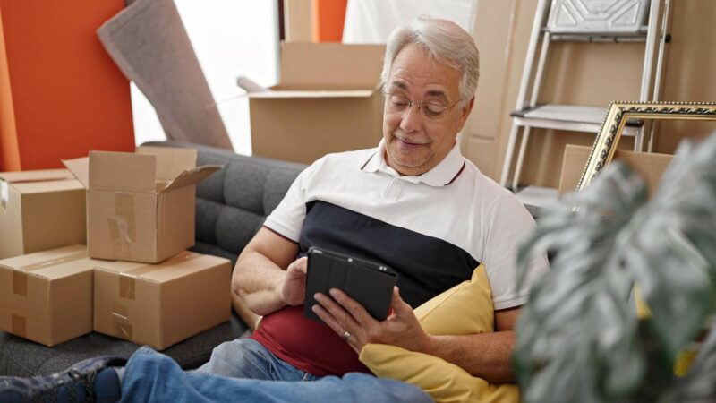 Un señor mayor se relaja con la tablet después de recoger en casas objetos de su casa. 