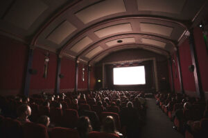Una sala de cine llena de personas y al fondo la pantalla en blanco.