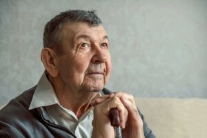 Primer plano de un Hombre mayor sentado, mirando hacia arriba mientras se apoya en un bastón.