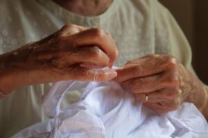 Una anciana cosiendo a mano una tela blanca.