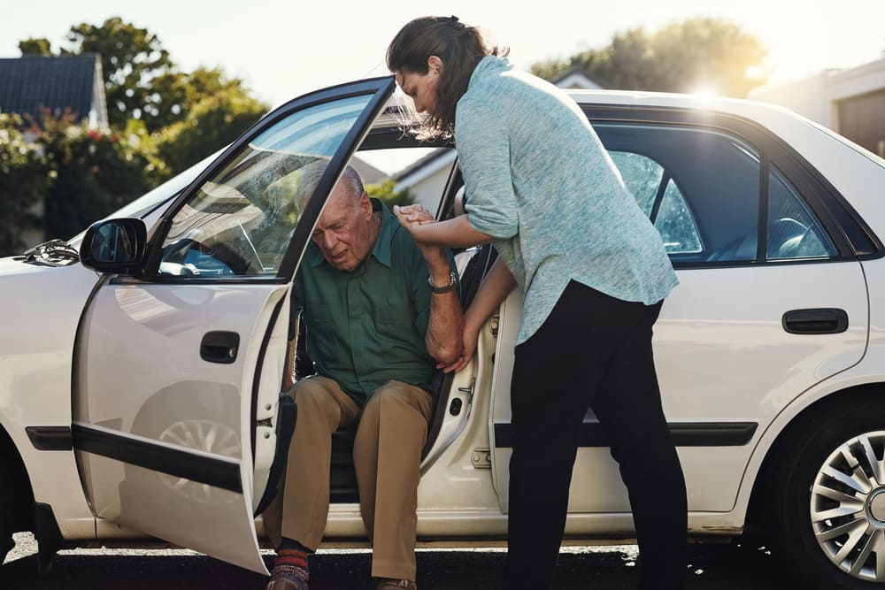 Una cuidadora ayuda a un anciano a salir de su coche. 